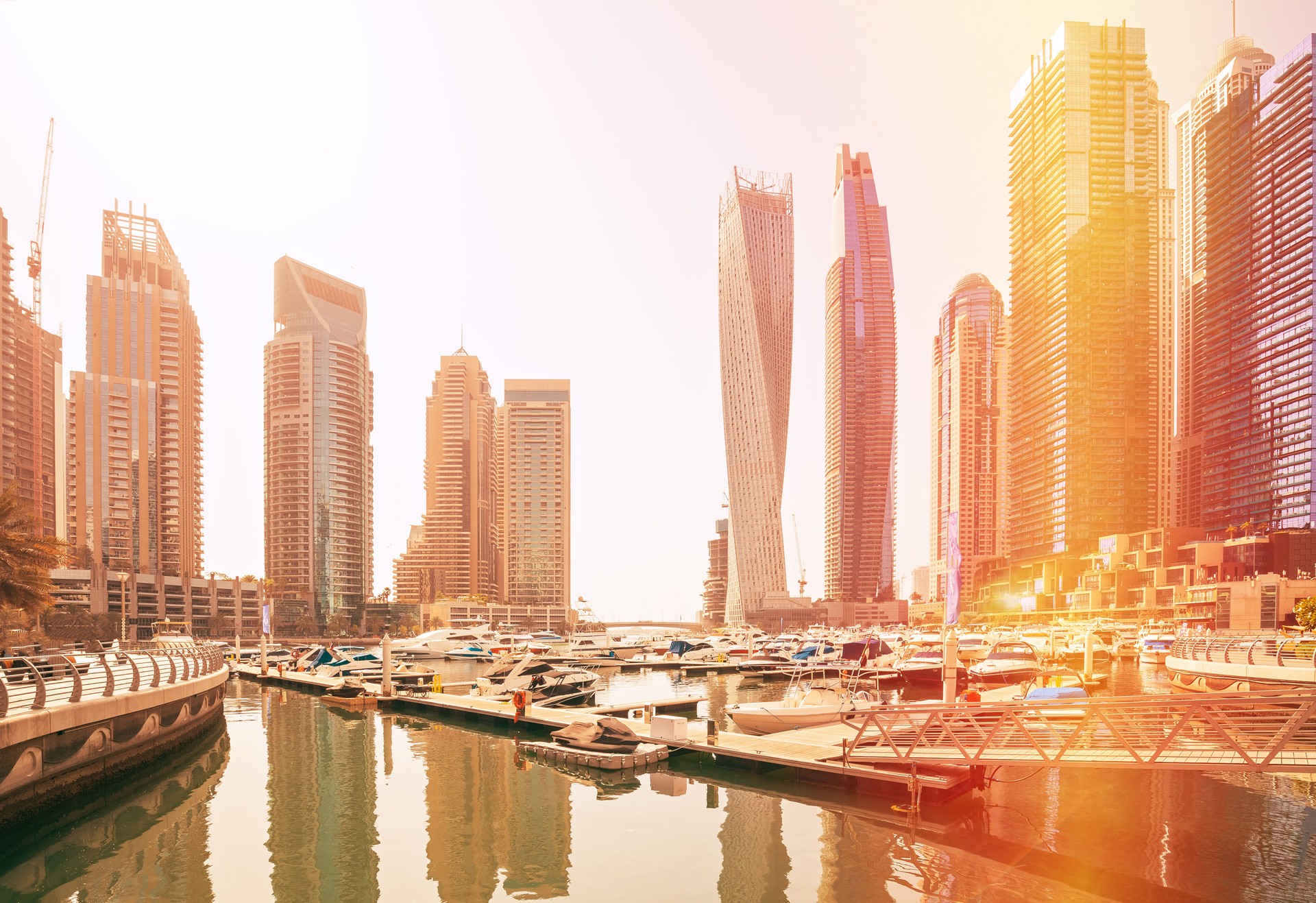 View of high-rise buildings of residential district in Dubai Marina and yachts moored near pier in sunny day. Dubai Marina Towers. Flare sun, film effect, lens flare, glow, film light, flare, highlight. High quality photo